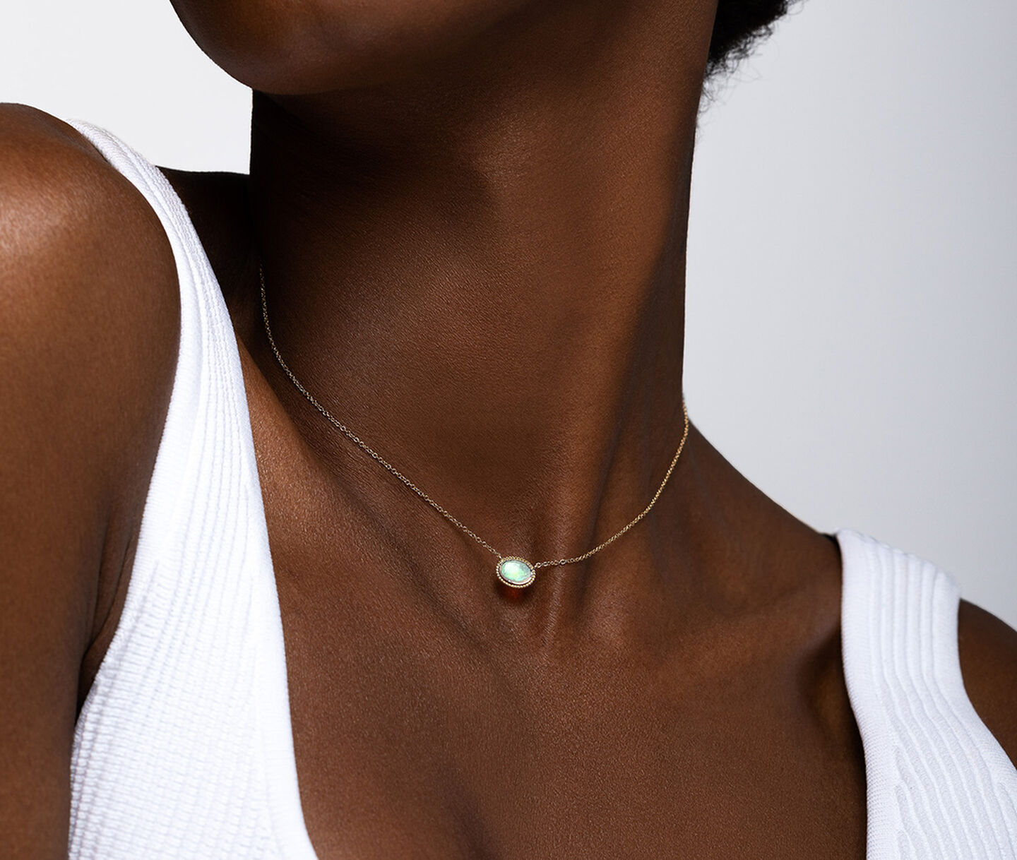 A woman wearing a Birks Essentials gold and opal pendant necklace.