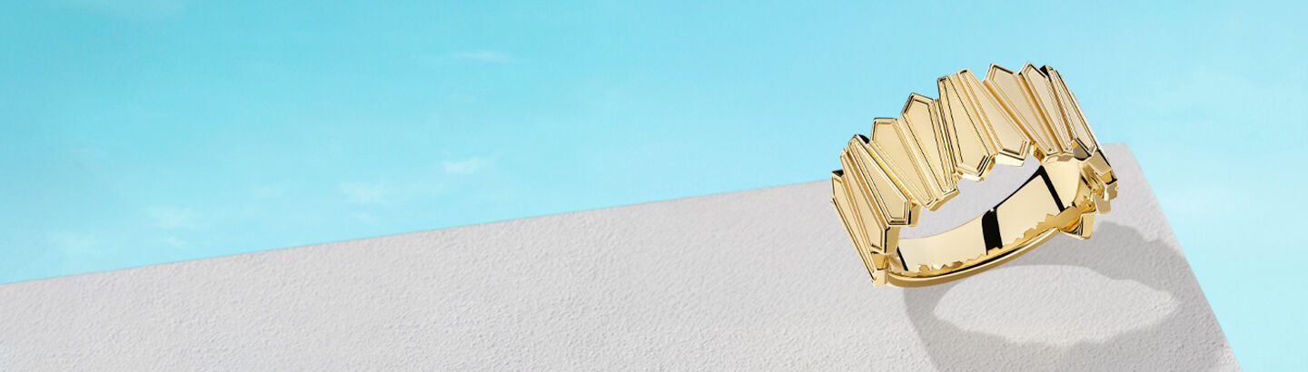 Birks Beekeeper yellow gold ring on a sky background.