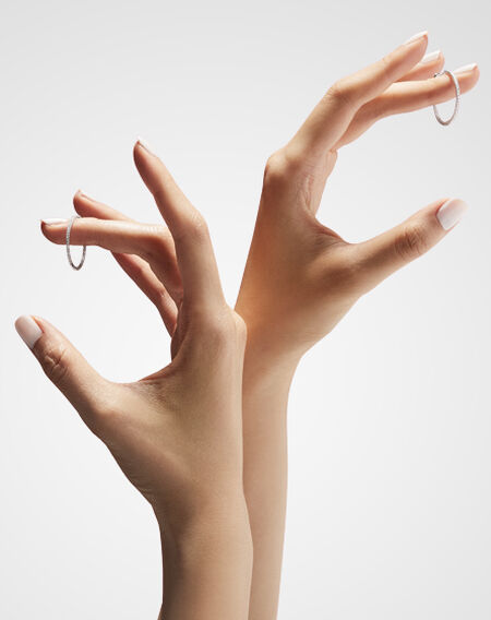 Women's hands holding a pair of Birks Essentials diamond hoop earrings