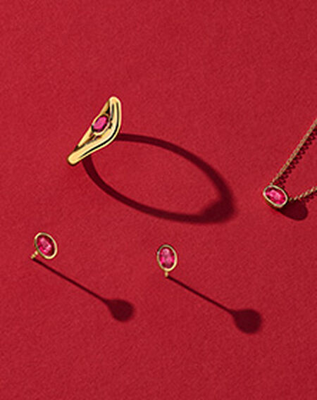 Birks Essentials gold and ruby jewellery on a red background.