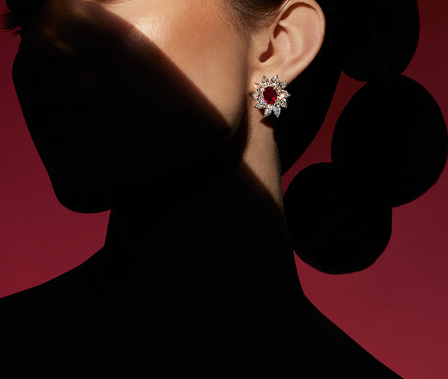 A woman wearing ruby high jewellery earrings by Maison Birks on a red background.