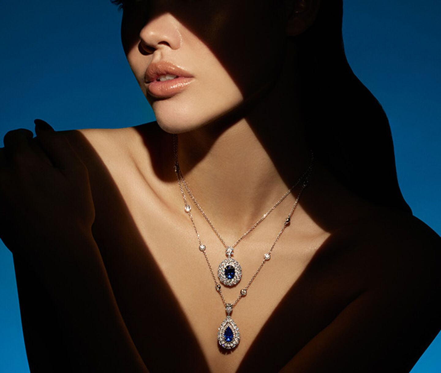 A woman wearing sapphire high jewellery necklaces by Maison Birks on a blue background.