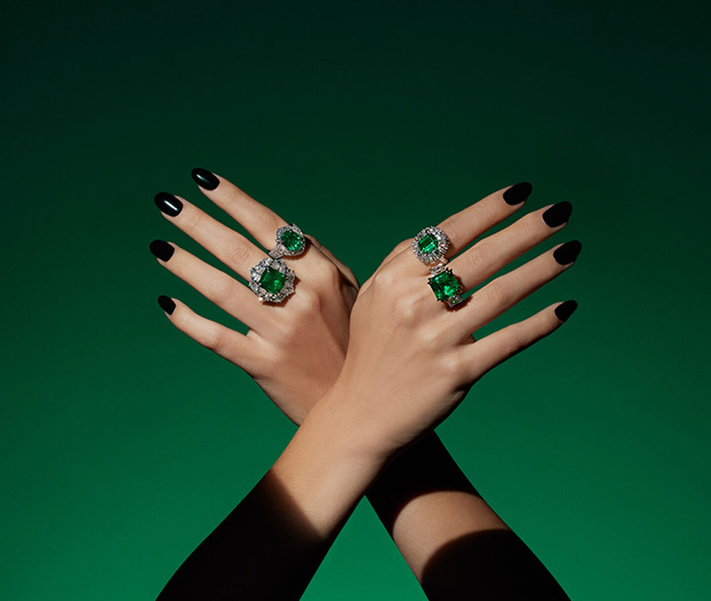 A hand wearing emerald high jewellery rings by Maison Birks on a green background.