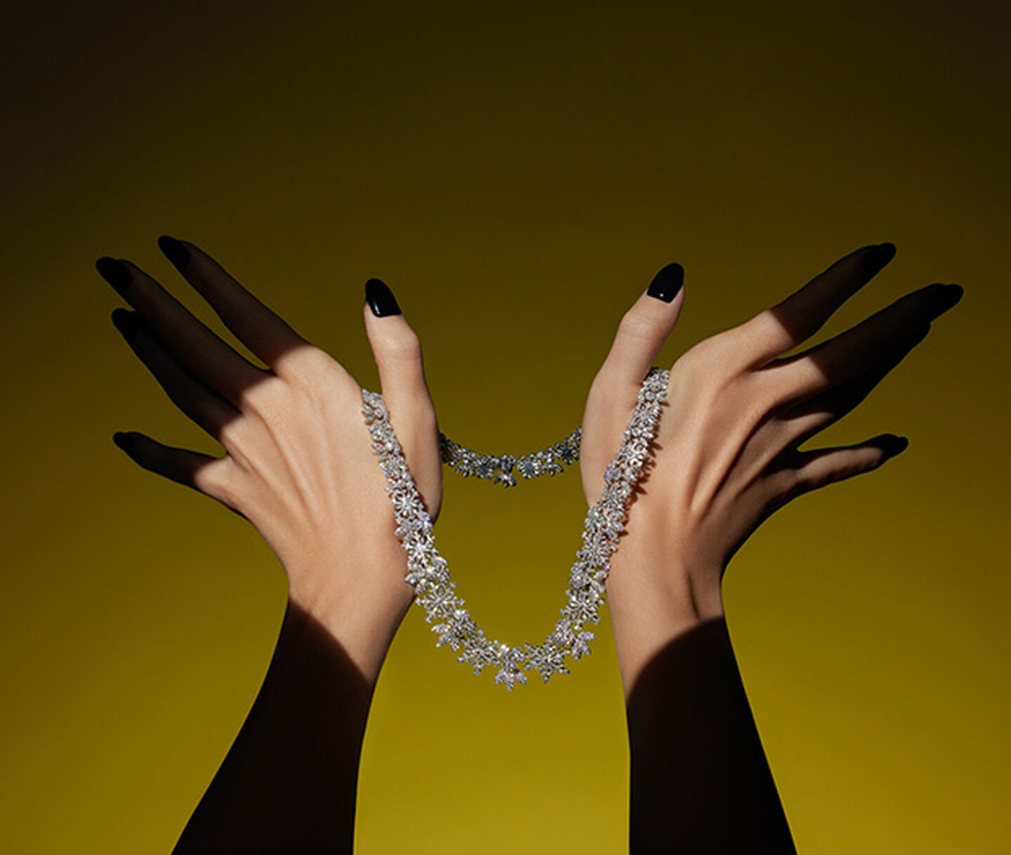 A woman's hand holding a diamond high jewellery necklace by Maison Birks on a yellow background.