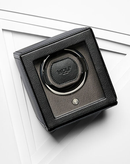 A black leather WOLF watch winder on a white layered background.