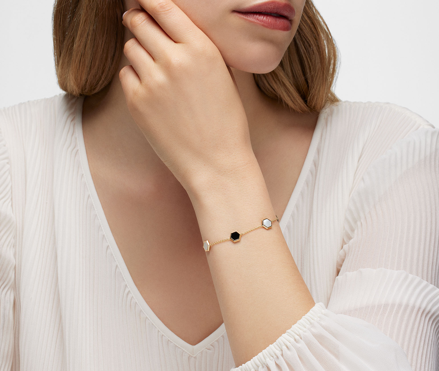 A woman wearing a Birks Bee Chic onyx and mother-of-pearl station bracelet.