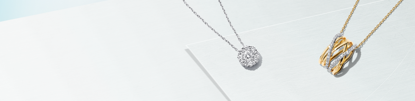 Birks round pendant with pave diamonds and Birks yellow gold and diamond pendant on a light blue background