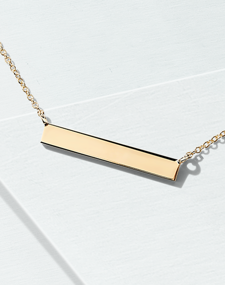 A Birks Essentials yellow gold bar necklace on a blueish background.