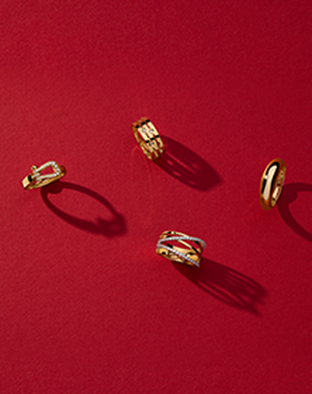Four gold rings from Maison Birks on a red background.