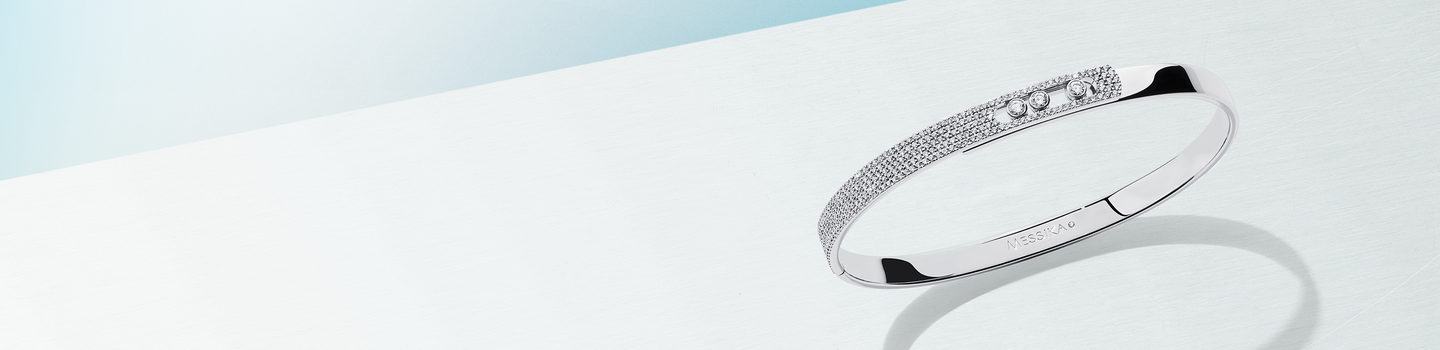 Messika Move Noa white gold and diamond bangle on a light blue background.