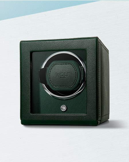 A green leather WOLF watch winder on a light blue background.